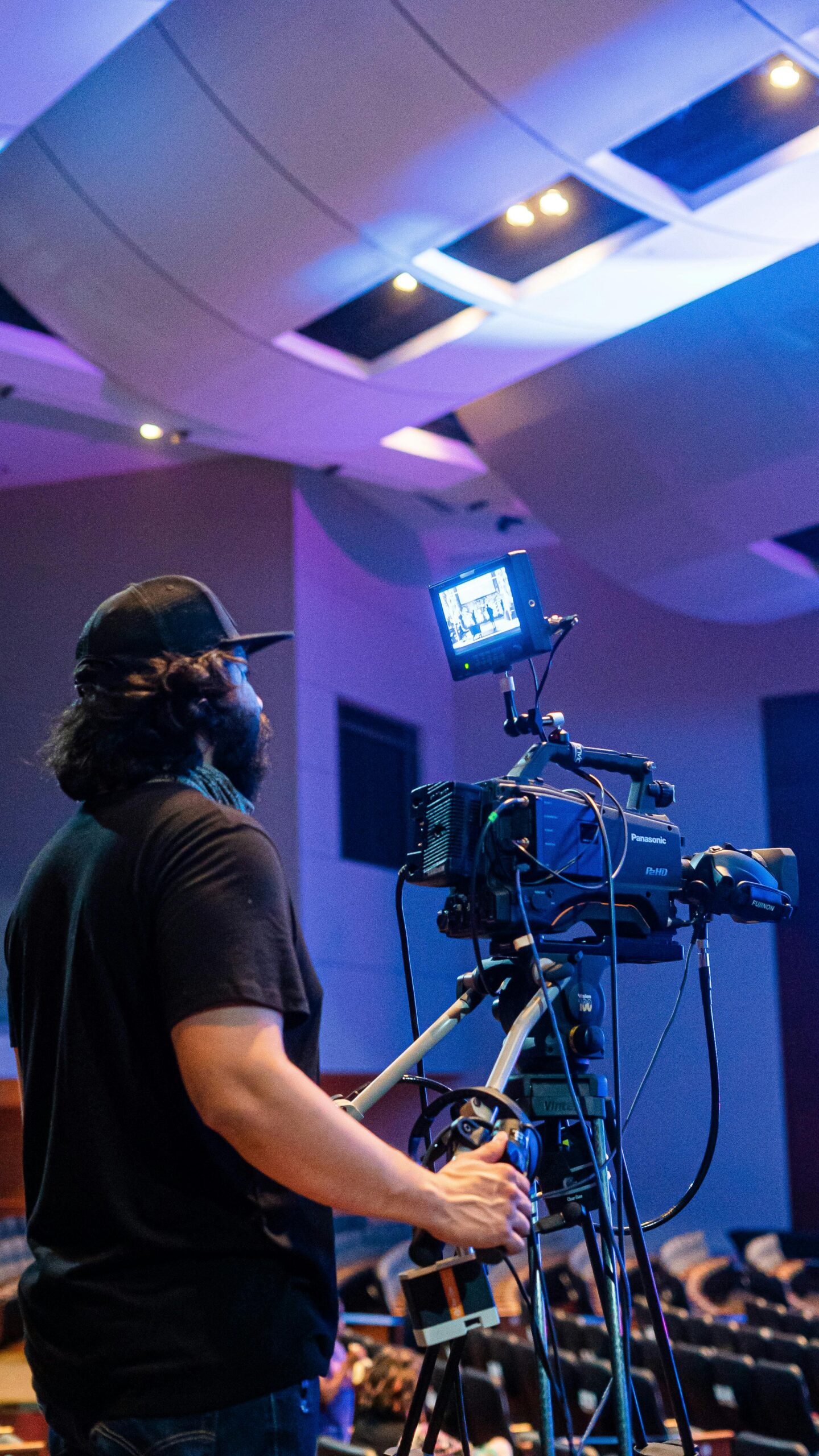 A videographer operates a camera capturing a large event indoors.